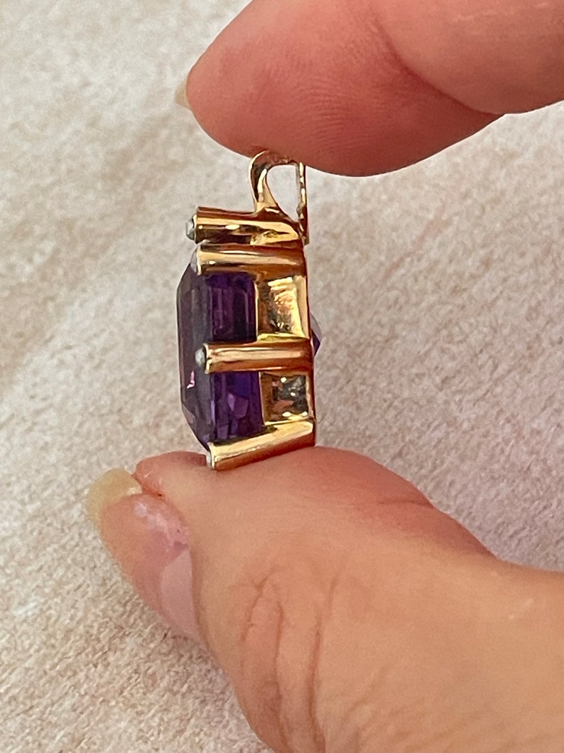 May include: A gold pendant featuring a large, faceted amethyst gemstone surrounded by smaller, clear gemstones. The pendant has a bail for attaching to a chain.