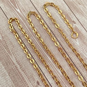 May include: Four gold chains of different lengths, laid out on a wooden surface.