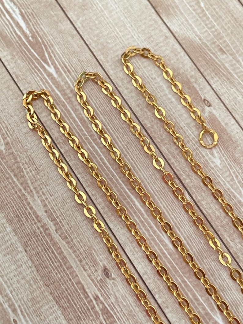 May include: Four gold chains of different lengths, laid out on a wooden surface.