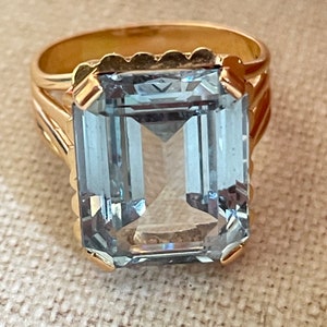 Könnte beinhalten: Ein goldener Ring mit einem großen, hellblauen, smaragdgeschliffenen Edelstein.