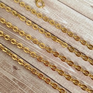 May include: A close-up of a gold chain necklace with multiple strands. The chain is made of oval-shaped links.