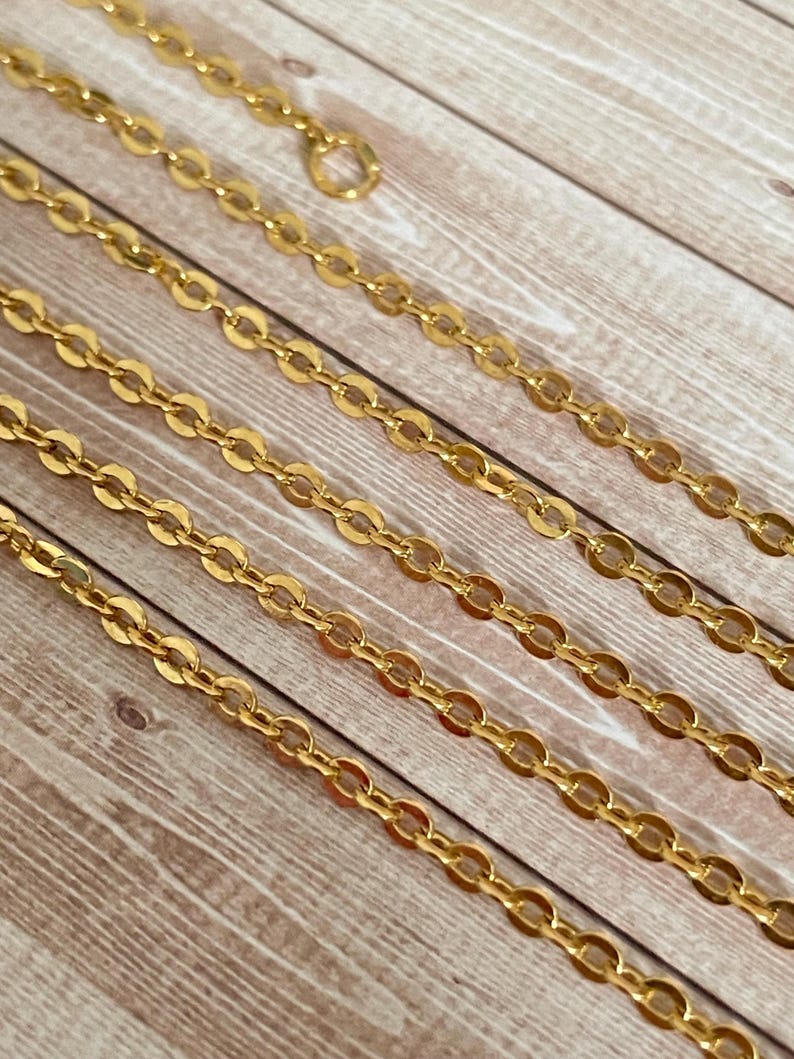 May include: A close-up of a gold chain necklace with multiple strands. The chain is made of oval-shaped links.