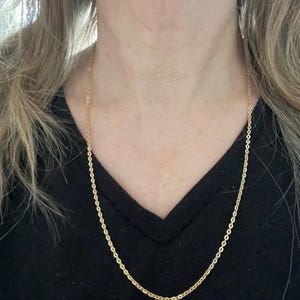 May include: A gold chain necklace on a person wearing a black shirt.