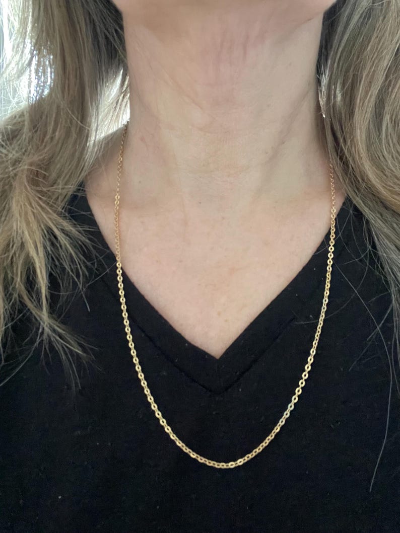 May include: A gold chain necklace on a person wearing a black shirt.