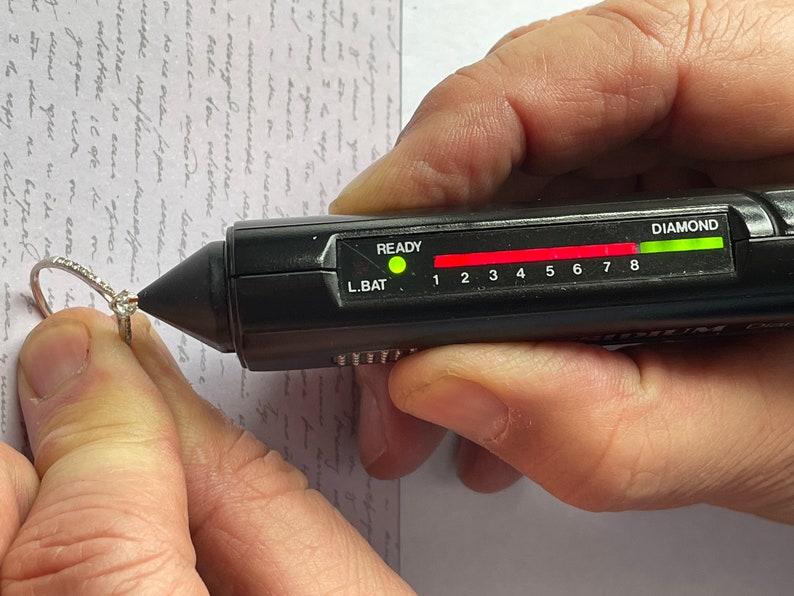 K&ouml;nnte beinhalten: Ein schwarzer Diamantentester mit einem gr&uuml;nen Licht, das anzeigt, dass ein Diamant vorhanden ist. Der Tester hat eine rote Leiste mit den Zahlen 1 bis 8 und die W&ouml;rter "READY" und "L.BAT" darauf.