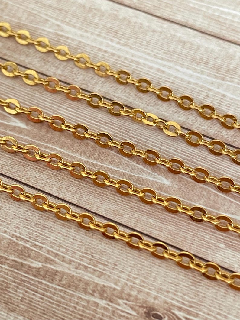May include: Four strands of gold chain on a wooden surface. The chain is made of small, oval-shaped links.