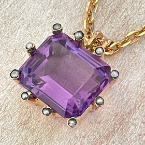 May include: A gold chain necklace with a pendant featuring a large, faceted amethyst gemstone surrounded by small pearls.