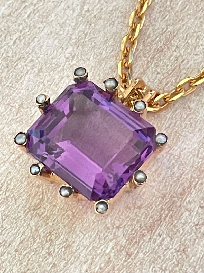 May include: A gold chain necklace with a pendant featuring a large, faceted amethyst gemstone surrounded by small pearls.