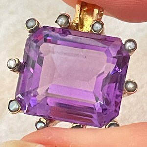 May include: A purple amethyst gemstone pendant set in gold with a border of small pearls.