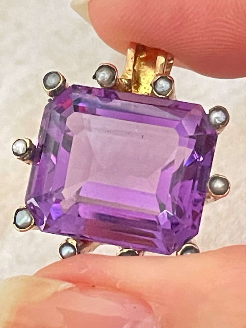May include: A purple amethyst gemstone pendant set in gold with a border of small pearls.
