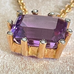May include: A gold pendant necklace with a large, rectangular amethyst gemstone surrounded by small, white pearls.