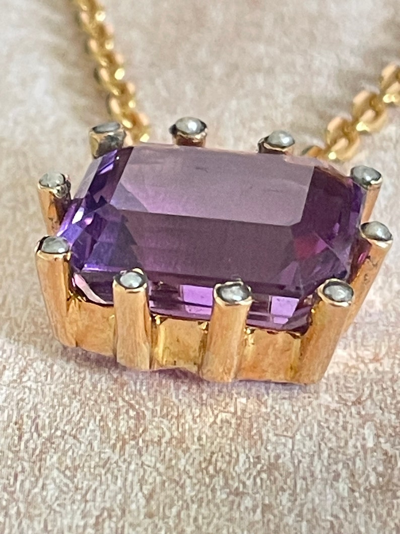 May include: A gold pendant necklace with a large, rectangular amethyst gemstone surrounded by small, white pearls.