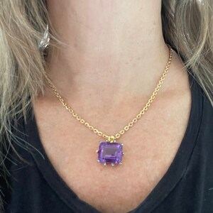 May include: A gold chain necklace with a purple gemstone pendant. The pendant is set in a gold frame with small diamonds around the edges.