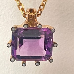 May include: A gold chain necklace with a pendant featuring a large, square-shaped amethyst gemstone surrounded by small pearl accents.