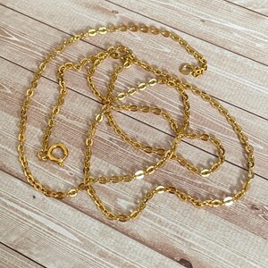 May include: A gold chain necklace with a lobster clasp closure. The chain is made of small, oval-shaped links.