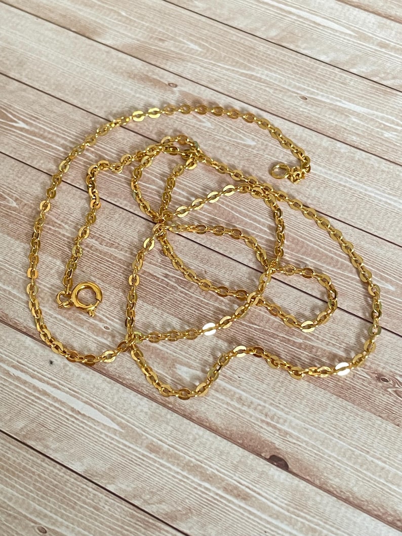 May include: A gold chain necklace with a lobster clasp closure. The chain is made of small, oval-shaped links.