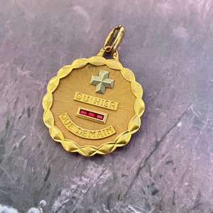 May include: Gold pendant with a white cross and red jewels. The pendant has the words "OU HIER QUE DEMAIN" inscribed on it.