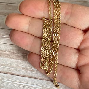 May include: A gold chain necklace with a delicate, oval-shaped link pattern. The chain is folded in half and held in a hand.
