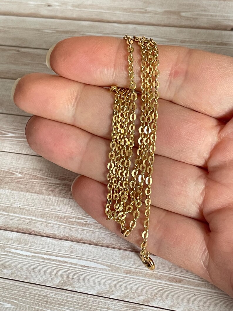 May include: A gold chain necklace with a delicate, oval-shaped link pattern. The chain is folded in half and held in a hand.