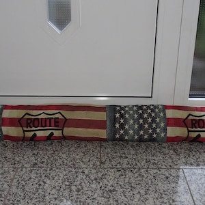 Può includere: Un fermaporta in tessuto con un design a bandiera americana rosso, bianco e blu. Il fermaporta ha la scritta "ROUTE" stampata.