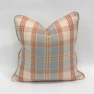 May include: A soft, cream-colored pillow with a light blue and orange plaid pattern. The pillow has a light gray trim around the edges.