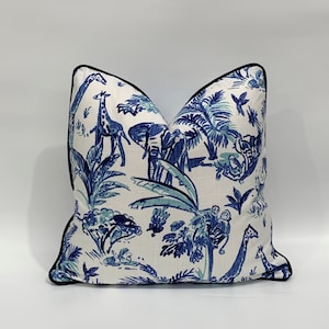 Könnte beinhalten: Ein weißes Kissen mit einem blauen und grünen Muster aus Tieren und Pflanzen. Das Kissen hat einen schwarzen Rand an den Kanten.