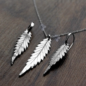 Op de afbeelding: Een zilveren ketting en oorbellenset met bladeren als hangers. De ketting heeft een delicate ketting en de oorbellen zijn van het druppeltype.