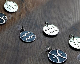 May include: Six silver charms featuring zodiac signs. The charms are round and have black and white enamel. The signs are Aquarius, Pisces, Capricorn, and Sagittarius.