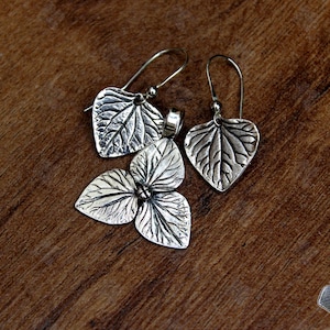 May include: A set of three silver earrings featuring a leaf design. The earrings are made of textured metal and have a delicate, organic look.