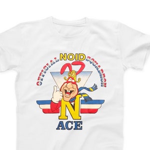 May include: White t-shirt with a cartoon character wearing a red and yellow costume. The character is giving a thumbs up and has a blue scarf. The text "OFFICIAL NOID SQUADRON #27 N ACE" is printed on the shirt.