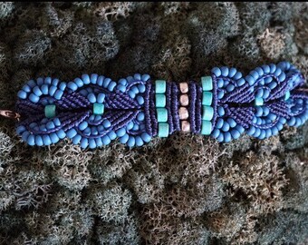 May include: A blue and turquoise beaded bracelet with a silver clasp. The bracelet is made using a macrame knotting technique.