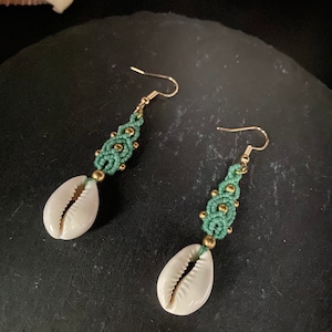 以下が含まれることがあります： カウリ貝のチャームが付いた、緑と金のマクラメのイヤリングのペアです。