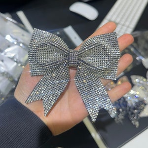 May include: A large silver bow made of rhinestones. The bow is about 6 inches wide and 4 inches tall.