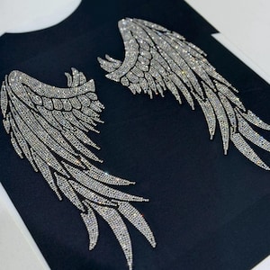 Op de afbeelding: Een zwart T-shirt met twee grote zilveren strass-engelenvleugels.