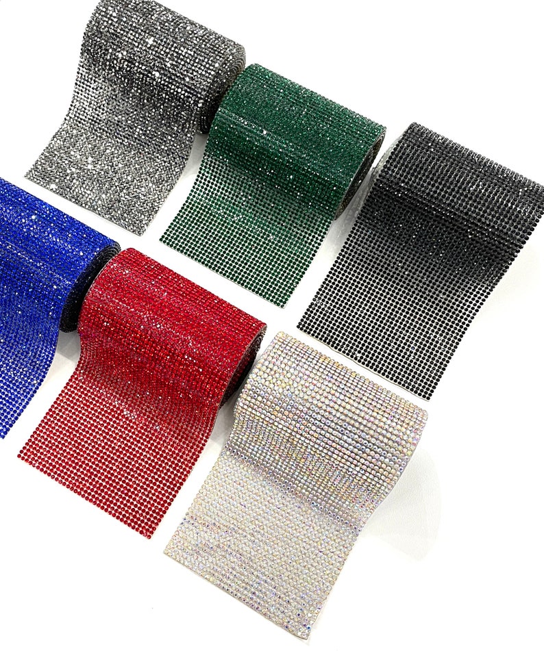 K&ouml;nnte beinhalten: Sechs Rollen Strassbesatz in verschiedenen Farben, darunter Silber, Gr&uuml;n, Schwarz, Blau, Rot und Klar. Jede Rolle ist etwa 3,8 cm breit und hat ein Gittermuster aus kleinen Strasssteinen.