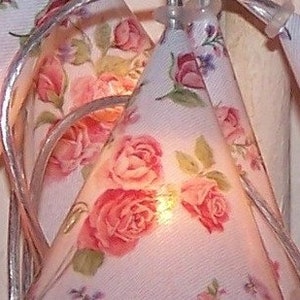 Könnte beinhalten: Eine Lichterkette mit weißen Stoffschirmen mit einem floralen Muster aus rosa Rosen und grünen Blättern. Die Lichter sind mit einem durchsichtigen Draht verbunden.
