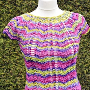 Può includere: Un top all'uncinetto con un motivo a righe colorate in tonalità di rosa, verde e viola. Il top ha maniche corte e una scollatura rotonda.