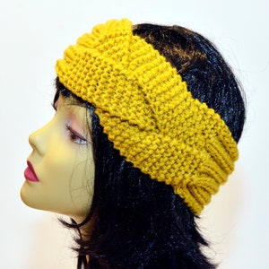 Può includere: Un cerchietto in maglia color giallo senape con un design intrecciato. Il cerchietto è indossato da un manichino con i capelli neri.