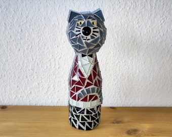 Può includere: Una statuetta di gatto in mosaico grigio con occhi gialli e un motivo a mosaico rosso, bianco e grigio sul corpo.