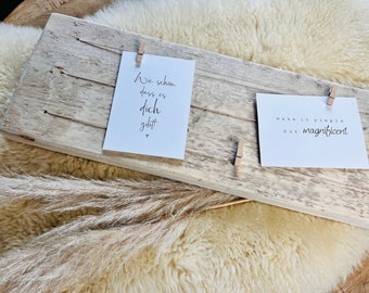 Puede incluir: Un marco de fotos de madera rústico con dos tarjetas blancas sujetas con pinzas de madera. Las tarjetas tienen mensajes escritos a mano: "Wie schön dass es dich gibt" y "make it simple but magnificent".