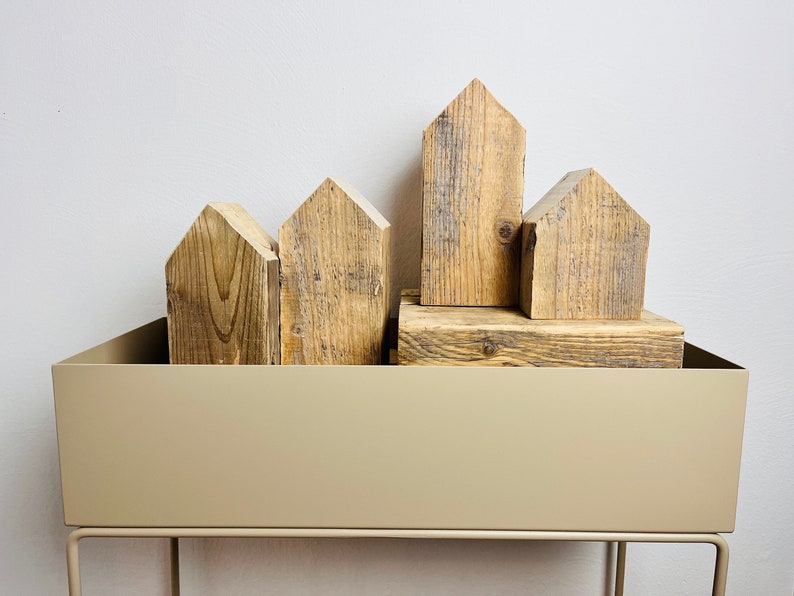 May include: A set of wooden house-shaped blocks arranged in a row on a beige metal shelf. The blocks are made of reclaimed wood and have a rustic, natural look.