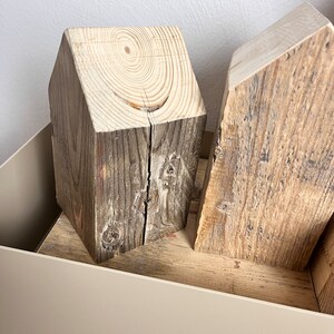 May include: Two wooden house-shaped blocks, one with a light brown finish and the other with a darker brown finish, are displayed in a light beige container.