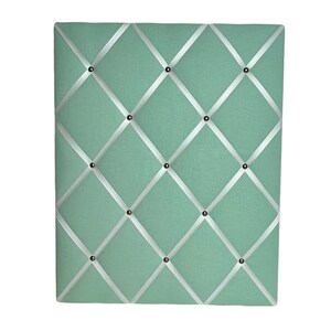 May include: A light green fabric bulletin board with white ribbon crisscrossing the surface and silver tacks.