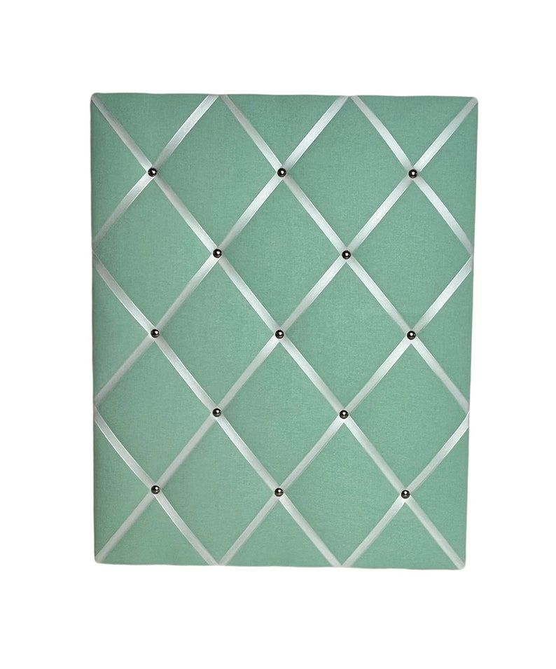 May include: A light green fabric bulletin board with white ribbon crisscrossing the surface and silver tacks.