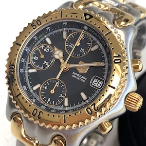 May include: A gold and silver chronograph wristwatch with a black face and three subdials. The watch has a date window at the 4 o'clock position and the words "automatic 200 metres" printed on the face.
