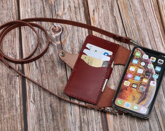 May include: A burgundy leather phone case with card slots and a brown leather strap. The case holds a smartphone with a black frame. The strap is attached to the case with metal clasps.