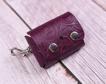 May include: A small, purple leather keychain with a floral embossed design. It has a silver clip and two silver snaps.