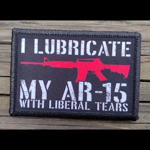 May include: Black patch with white text that reads "I lubricate my AR-15 with liberal tears". A red silhouette of an AR-15 rifle is in the center of the patch.