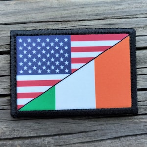 May include: Rectangular patch featuring a split design: the upper left displays the American flag, and the lower right shows the Irish flag. The patch is bordered with black stitching and set against a wooden surface.