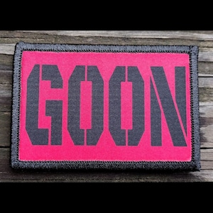 May include: A rectangular patch with the word "GOON" in large, stencil-style black letters on a bright pink background. The patch has a black border and is likely made of fabric.